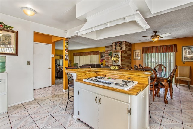 kitchen with white gas cooktop, a textured ceiling, white cabinets, a kitchen breakfast bar, and ceiling fan