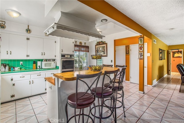 kitchen with white cabinets, a textured ceiling, backsplash, and oven