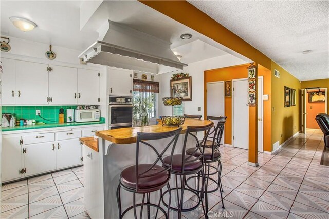 15937 Manzanita Dr, Fontana, CA 92335 - kitchen with white cabinetry, a kitchen breakfast bar, tile counters, and light tile patterned flooring