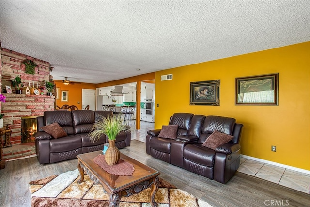 living room with ceiling fan, a textured ceiling, a fireplace, and hardwood / wood-style floors