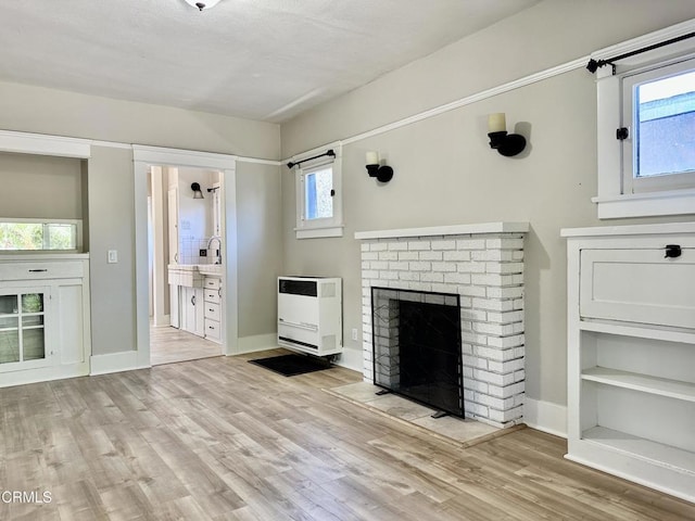 unfurnished living room featuring plenty of natural light, a fireplace, light hardwood / wood-style flooring, and heating unit