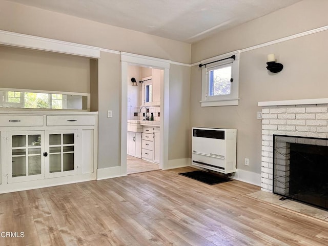 unfurnished living room with heating unit, a brick fireplace, and light hardwood / wood-style floors