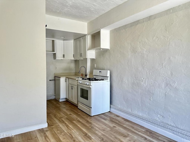 kitchen with white cabinets, white gas range, sink, and light hardwood / wood-style flooring