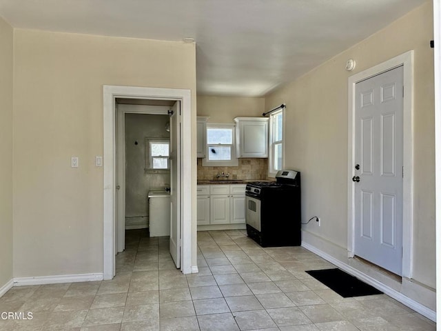 kitchen with sink, decorative backsplash, black gas range oven, light tile patterned flooring, and white cabinetry