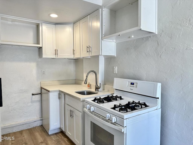 kitchen featuring white range with gas cooktop, white cabinetry, sink, and light hardwood / wood-style flooring