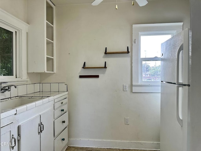 kitchen featuring white cabinets, sink, ceiling fan, tile counters, and white fridge