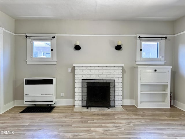 unfurnished living room with heating unit, a brick fireplace, and light wood-type flooring