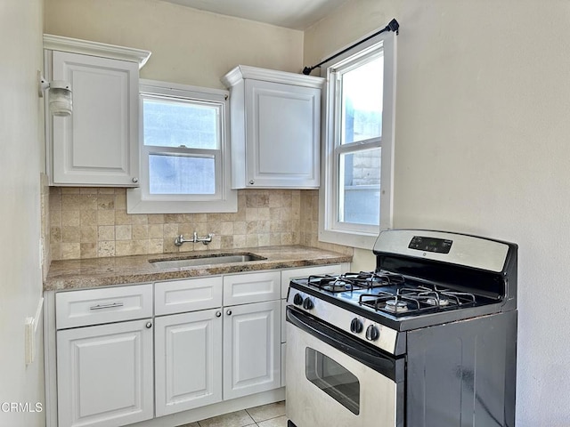 kitchen featuring sink, light tile patterned floors, stainless steel range with gas cooktop, decorative backsplash, and white cabinets