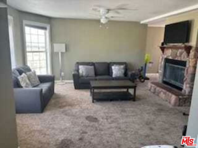 living room featuring carpet, a stone fireplace, and ceiling fan