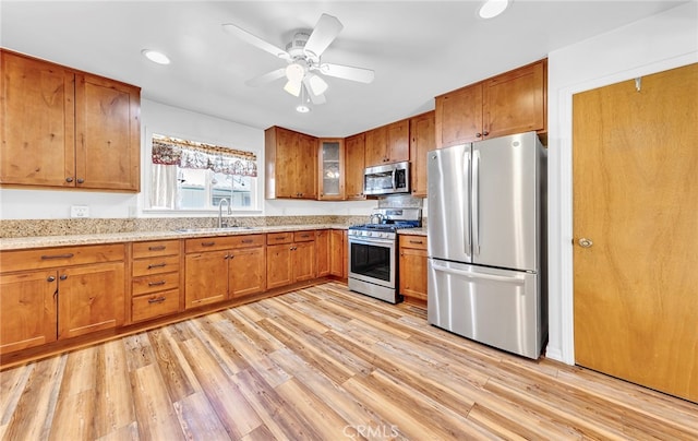 kitchen with light stone countertops, stainless steel appliances, light wood-type flooring, ceiling fan, and sink