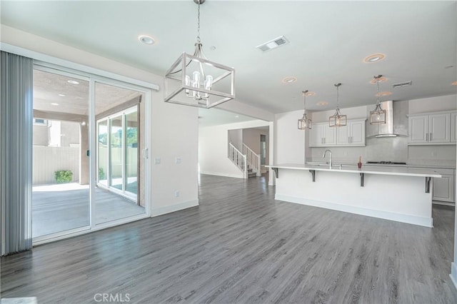 kitchen featuring pendant lighting, a center island with sink, wall chimney range hood, dark hardwood / wood-style floors, and white cabinetry