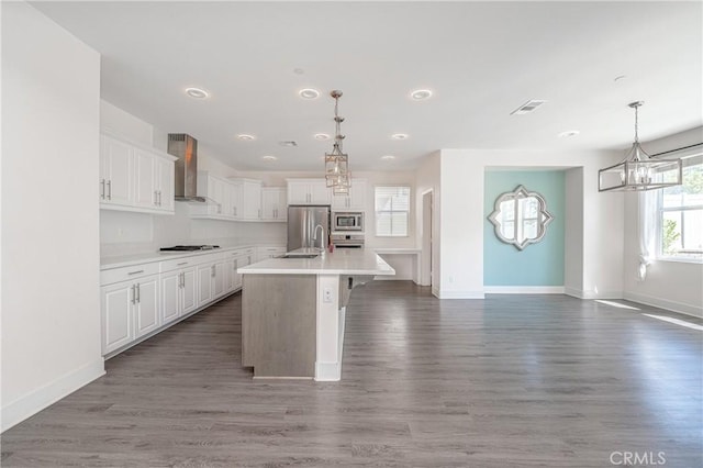 kitchen featuring appliances with stainless steel finishes, dark hardwood / wood-style flooring, wall chimney exhaust hood, a center island with sink, and white cabinetry