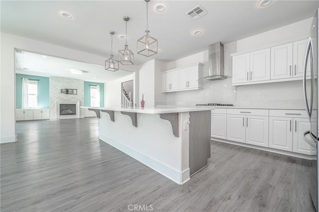 kitchen with white cabinetry, wall chimney range hood, gas cooktop, a breakfast bar, and a center island with sink