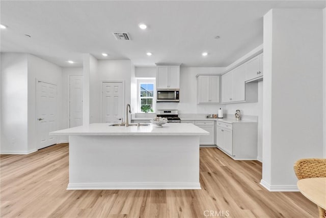 kitchen featuring appliances with stainless steel finishes, sink, light hardwood / wood-style flooring, white cabinetry, and an island with sink