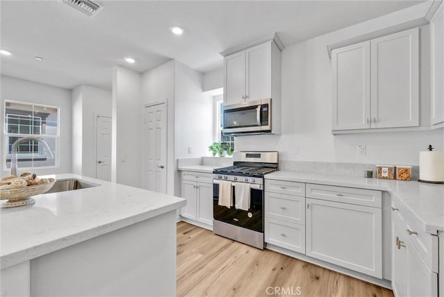 kitchen with sink, light wood-type flooring, appliances with stainless steel finishes, light stone counters, and white cabinetry