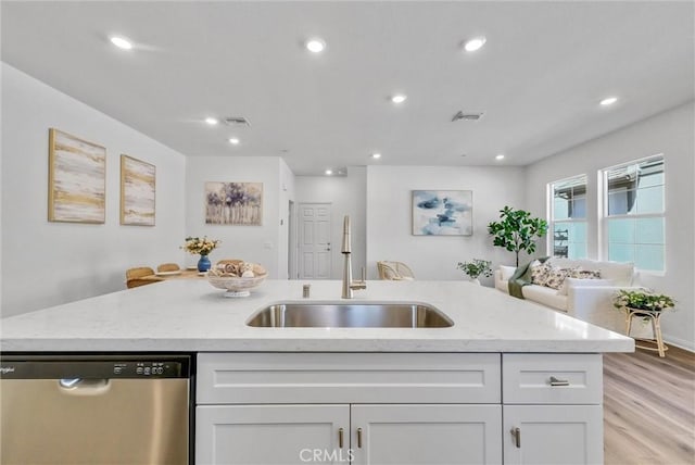 kitchen featuring white cabinetry, dishwasher, sink, light hardwood / wood-style flooring, and a center island with sink