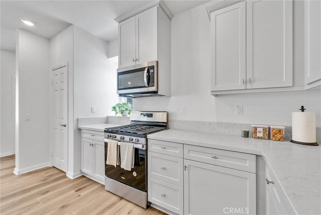 kitchen featuring white cabinets, stainless steel appliances, light hardwood / wood-style flooring, and light stone counters