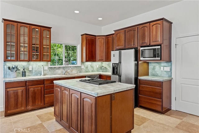 kitchen with sink, appliances with stainless steel finishes, a center island, light stone countertops, and decorative backsplash