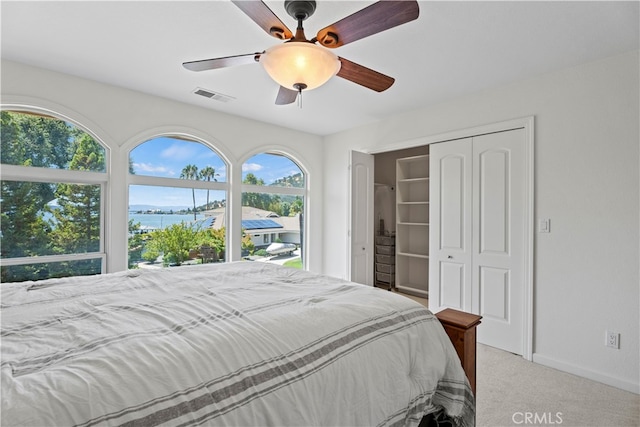 carpeted bedroom featuring a water view, ceiling fan, and a closet