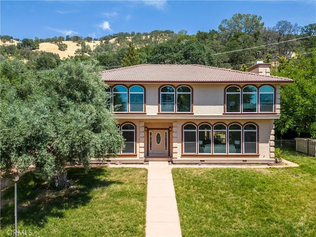 mediterranean / spanish-style house with a chimney, a front yard, a tile roof, and stucco siding