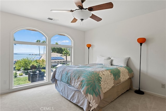 carpeted bedroom featuring multiple windows, a water view, and ceiling fan