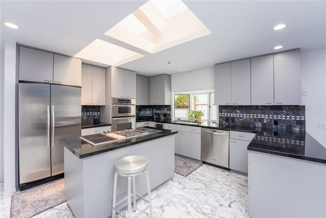 kitchen with gray cabinetry, decorative backsplash, a kitchen island, and stainless steel appliances