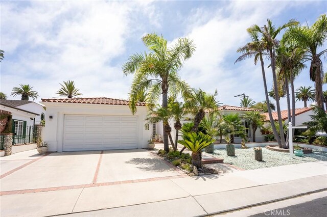 mediterranean / spanish-style house with an attached garage, a tiled roof, concrete driveway, and stucco siding