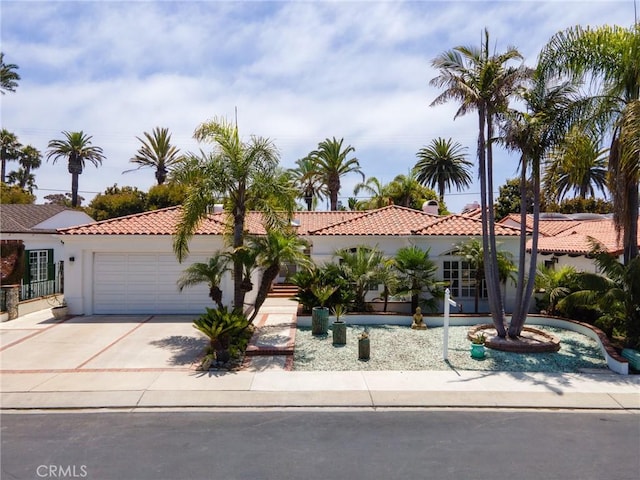 mediterranean / spanish home with a garage, stucco siding, a tiled roof, and driveway