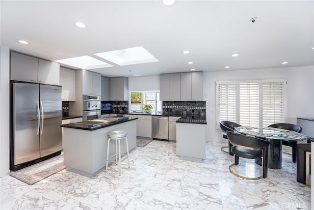 kitchen featuring a center island, a skylight, gray cabinets, tasteful backsplash, and stainless steel appliances