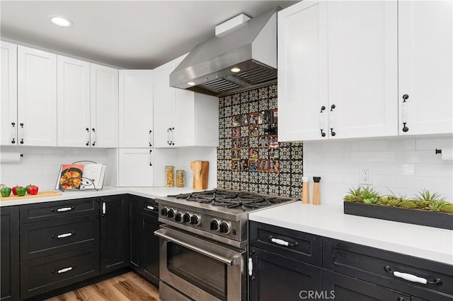 kitchen with tasteful backsplash, light hardwood / wood-style floors, high end stainless steel range, and wall chimney range hood