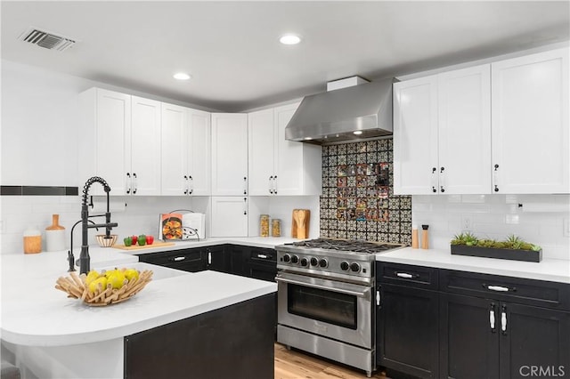 kitchen featuring wall chimney exhaust hood, high end stove, backsplash, white cabinets, and light wood-type flooring