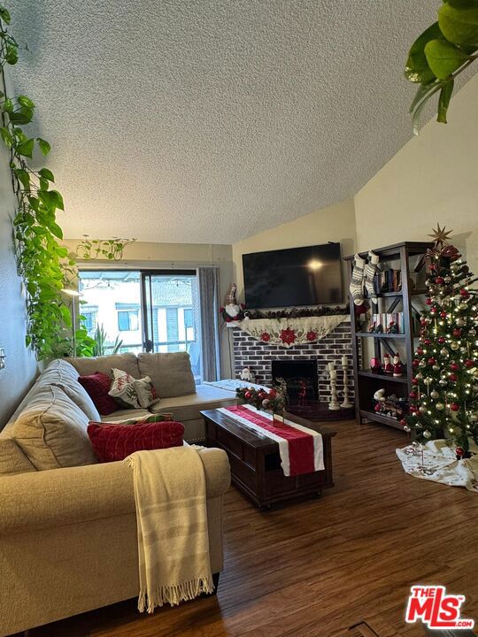 living room featuring a fireplace, dark hardwood / wood-style flooring, a textured ceiling, and vaulted ceiling