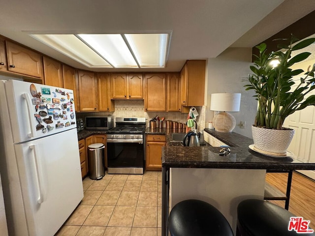 kitchen with sink, light tile patterned floors, a kitchen bar, kitchen peninsula, and stainless steel appliances