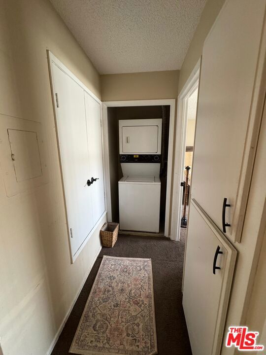 hall featuring dark colored carpet, a textured ceiling, and stacked washing maching and dryer