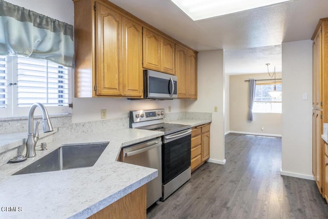 kitchen with wood-type flooring, sink, hanging light fixtures, and stainless steel appliances