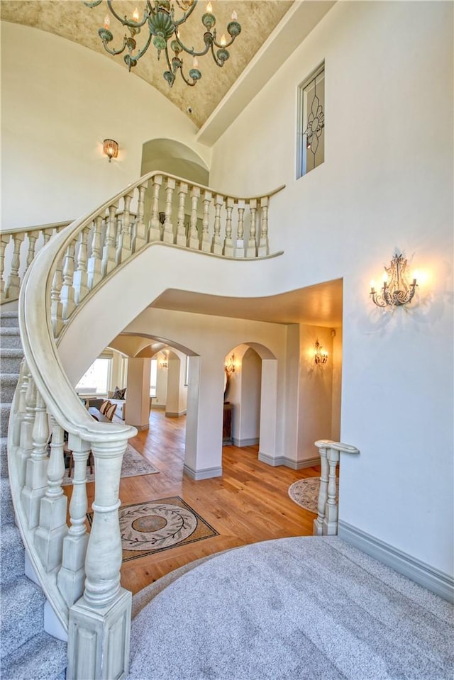 stairs with high vaulted ceiling, baseboards, arched walkways, and wood finished floors