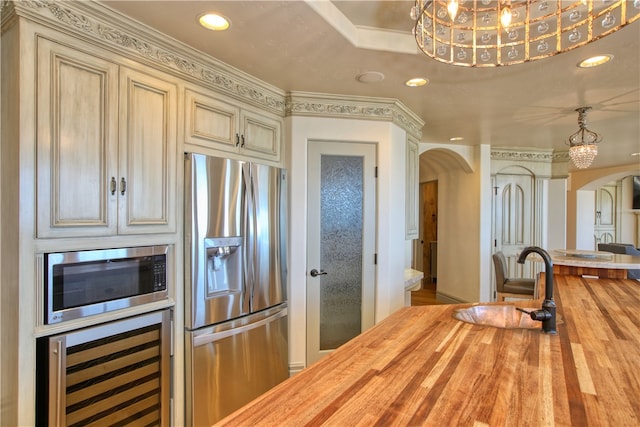 kitchen with wine cooler, butcher block counters, stainless steel appliances, cream cabinets, and a chandelier