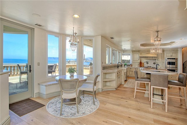 dining room with a water view, light wood-style flooring, visible vents, and an inviting chandelier