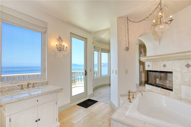 full bathroom featuring a garden tub, a water view, a tiled fireplace, wood finished floors, and baseboards