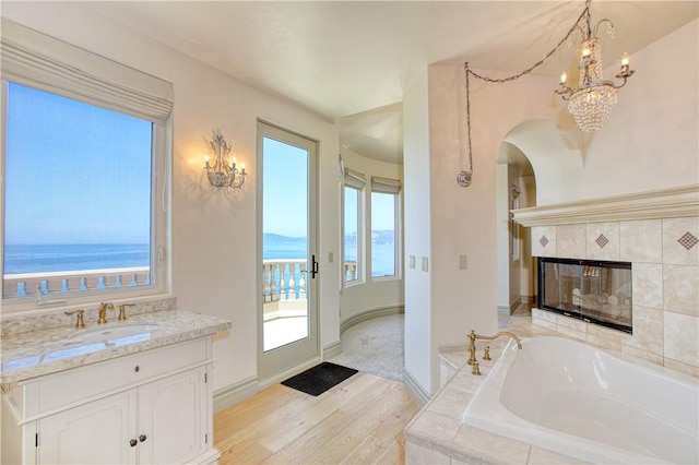 bathroom featuring a notable chandelier, baseboards, a fireplace, a garden tub, and wood finished floors