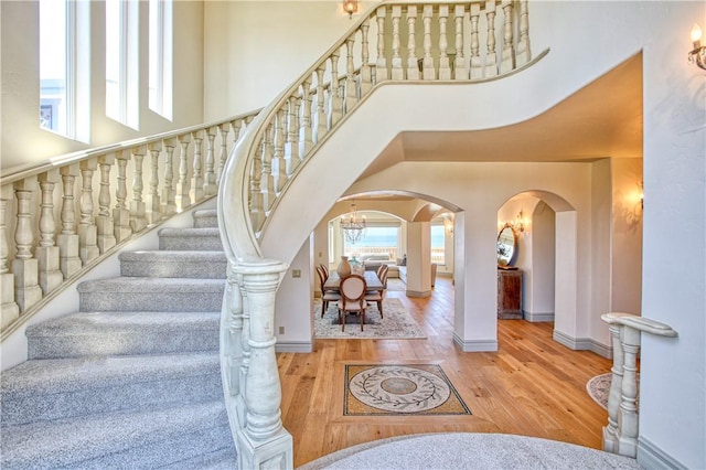 stairs with arched walkways, baseboards, a high ceiling, and wood finished floors