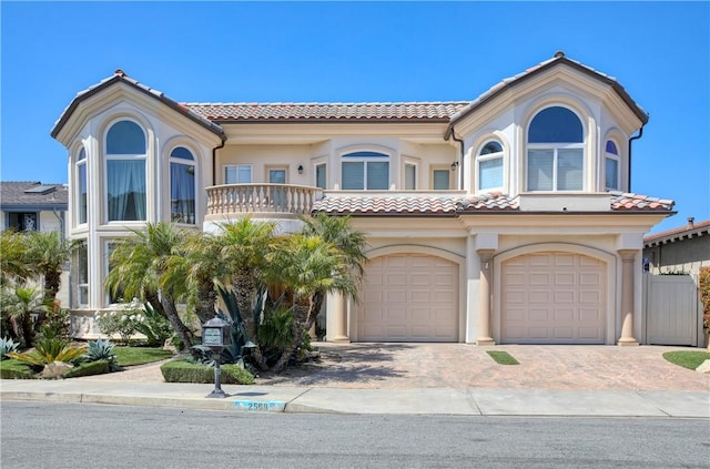 mediterranean / spanish-style house with a tiled roof, an attached garage, a balcony, stucco siding, and decorative driveway