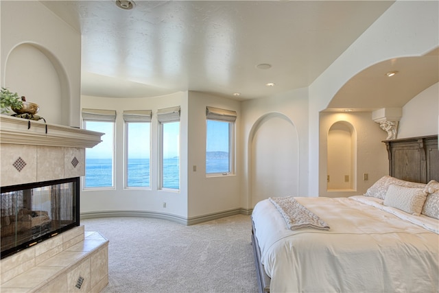 bedroom with light carpet, a tiled fireplace, and a water view