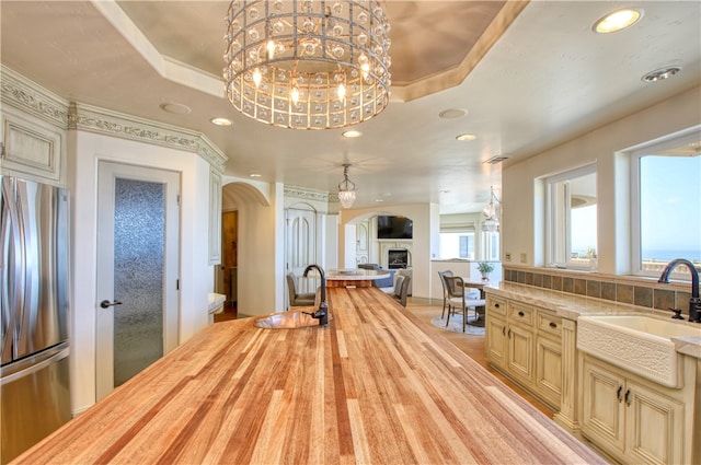 kitchen featuring a tray ceiling, cream cabinets, freestanding refrigerator, a sink, and butcher block countertops