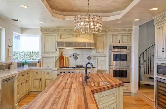 kitchen with butcher block countertops, a tray ceiling, stainless steel appliances, and cream cabinetry