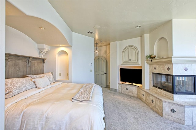 bedroom with arched walkways, a tile fireplace, light carpet, and visible vents