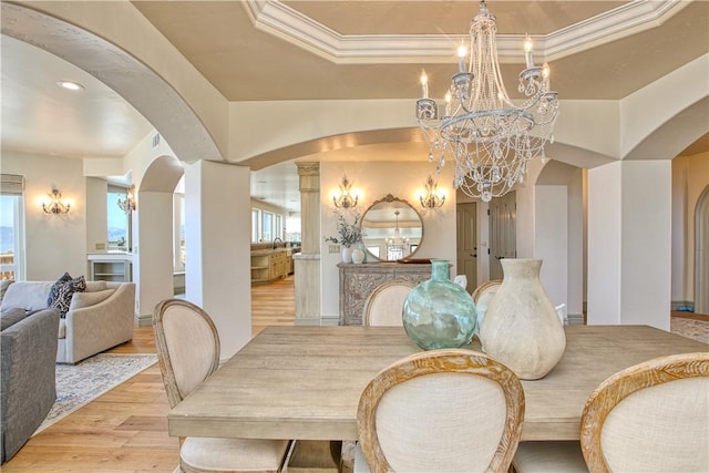 dining space with crown molding, light wood-style flooring, arched walkways, and a chandelier