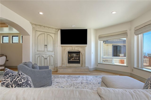 living room featuring arched walkways, recessed lighting, a premium fireplace, baseboards, and light wood-type flooring