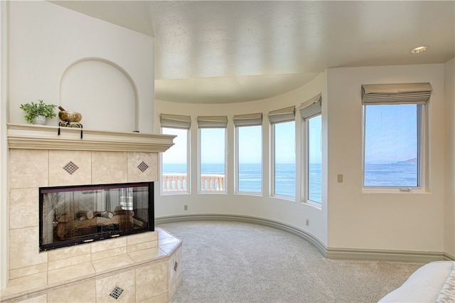 carpeted living area featuring baseboards, a water view, and a tiled fireplace