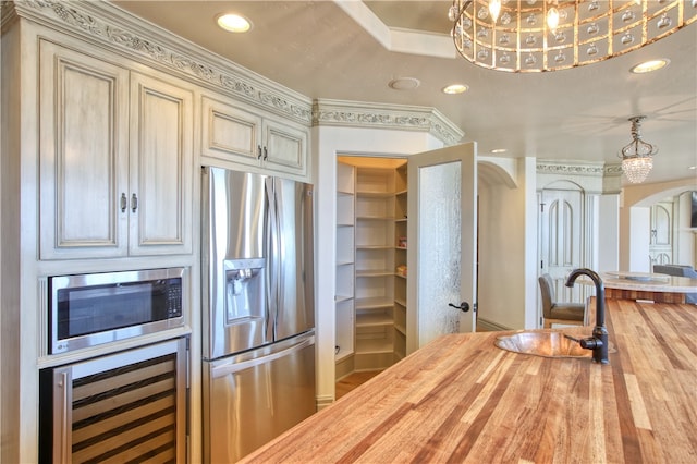 kitchen featuring beverage cooler, arched walkways, wood counters, appliances with stainless steel finishes, and recessed lighting